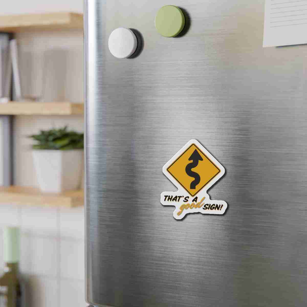 Close-up of a brushed stainless steel fridge with two magnets and a humorous yellow road-sign sticker reading "That's a road sign!" in a kitchen.